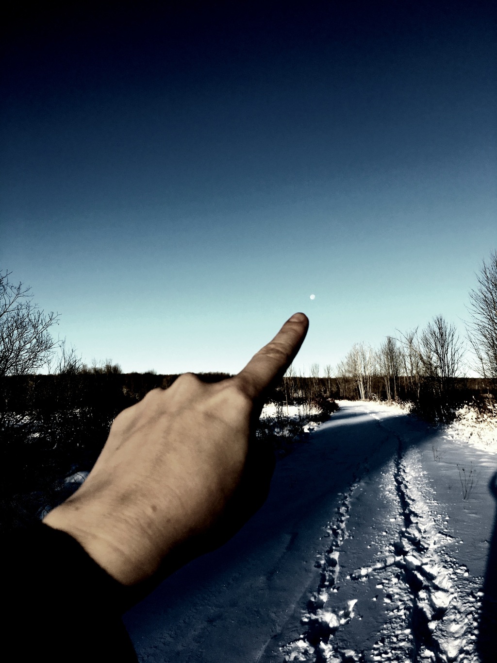 Finger pointing to the moon in the sky with a snowy trail in the background